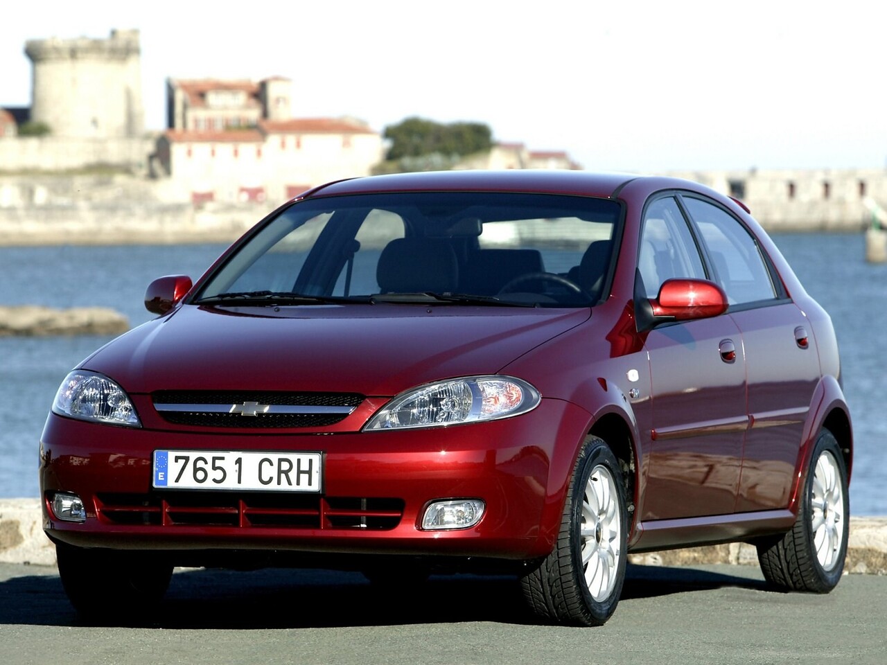 Chevrolet Lacetti хэтчбек 5-дв. (I поколение, 2004 - 2013 г.в.): Красный хэтчбек у каменного здания у моря