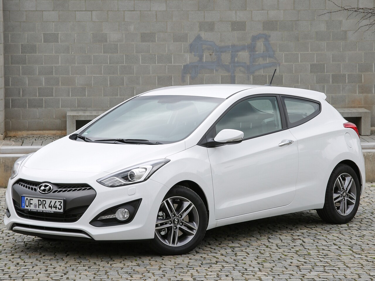 Hyundai i30 хэтчбек 3-дв. 1.6 AT Classic: Белый трёхдверный хэтчбек на брусчатке у каменной стены, вид спереди сбоку