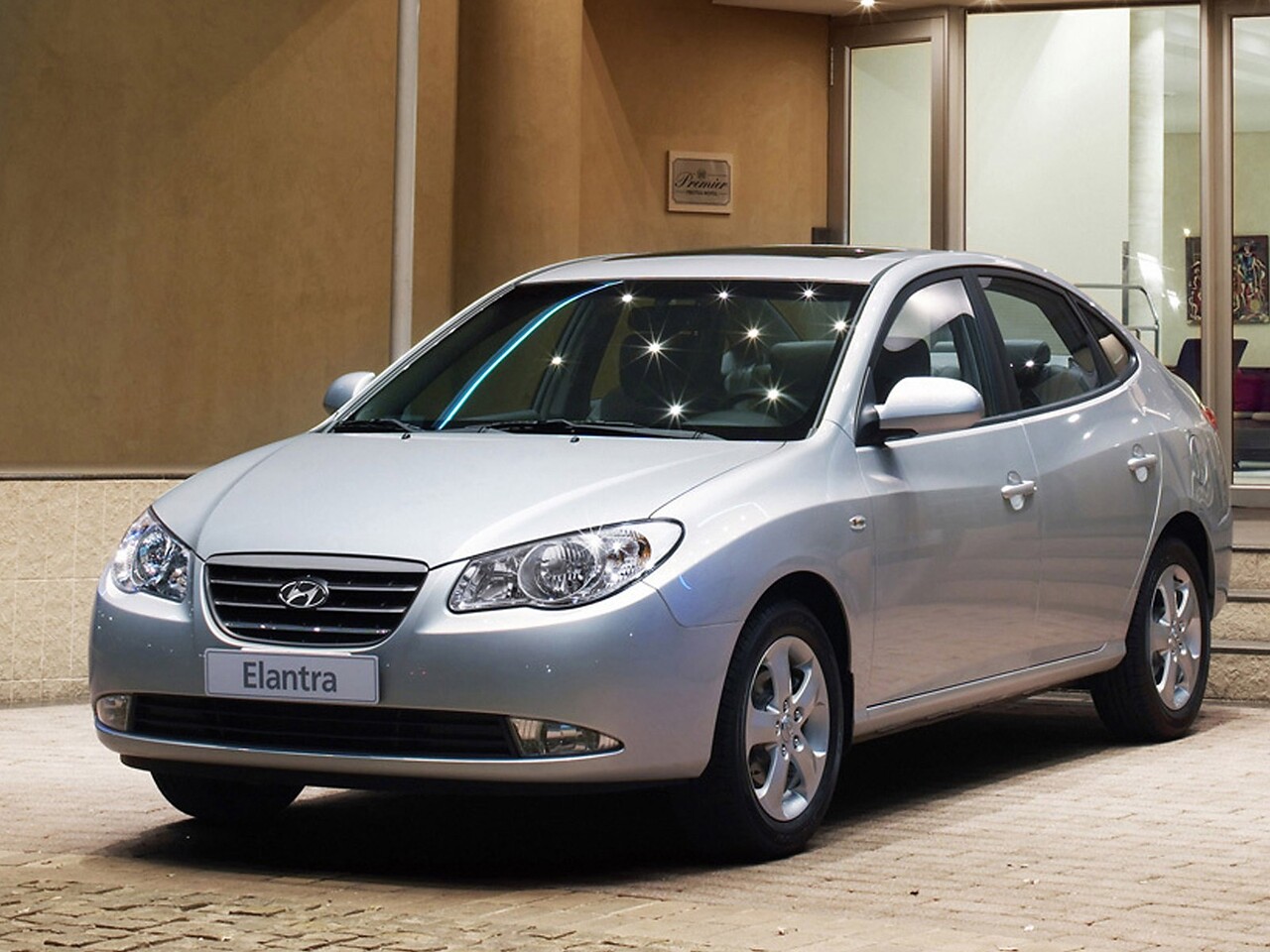 Hyundai Elantra (IV поколение, 2006 - 2008 г.в.): Серебристый седан у современного здания, вид спереди сбоку