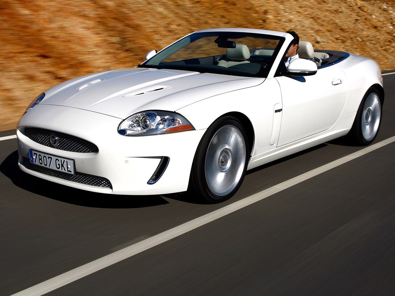 Jaguar XK R Кабриолет (III поколение, 2006 - 2012 г.в.): Три четверти спереди в движении у скалистого склона
