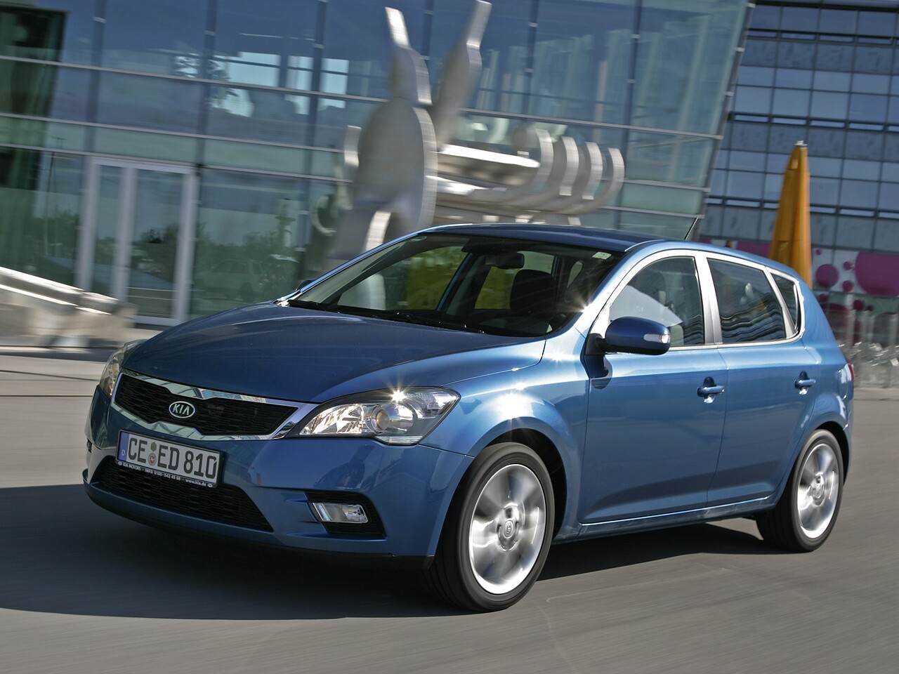 KIA Ceed Хэтчбек (I поколение, рестайлинг, 2010 - 2012 г.в.): Три четверти спереди в движении у стеклянного здания