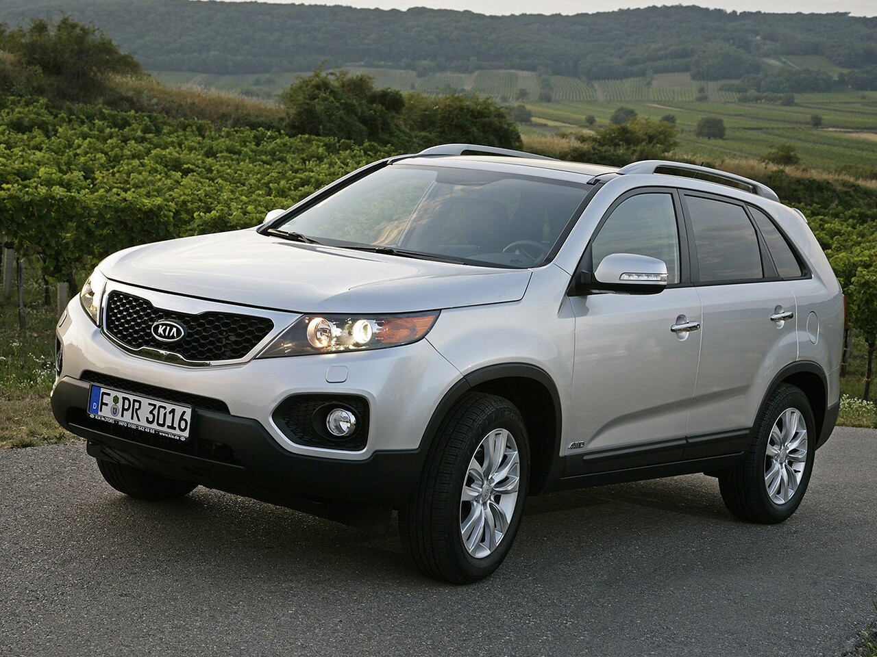 KIA Sorento (II поколение, 2009 - 2012 г.в.): Три четверти спереди на дороге в холмах