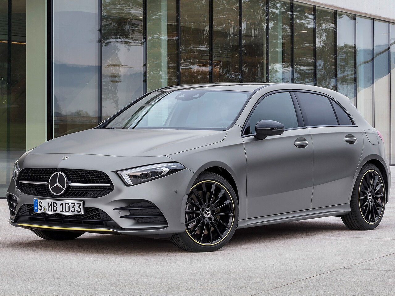 Mercedes-Benz A-Класс хэтчбек 5-дв. 1.3 AT Sport: Серый хэтчбек у современного здания, вид спереди сбоку