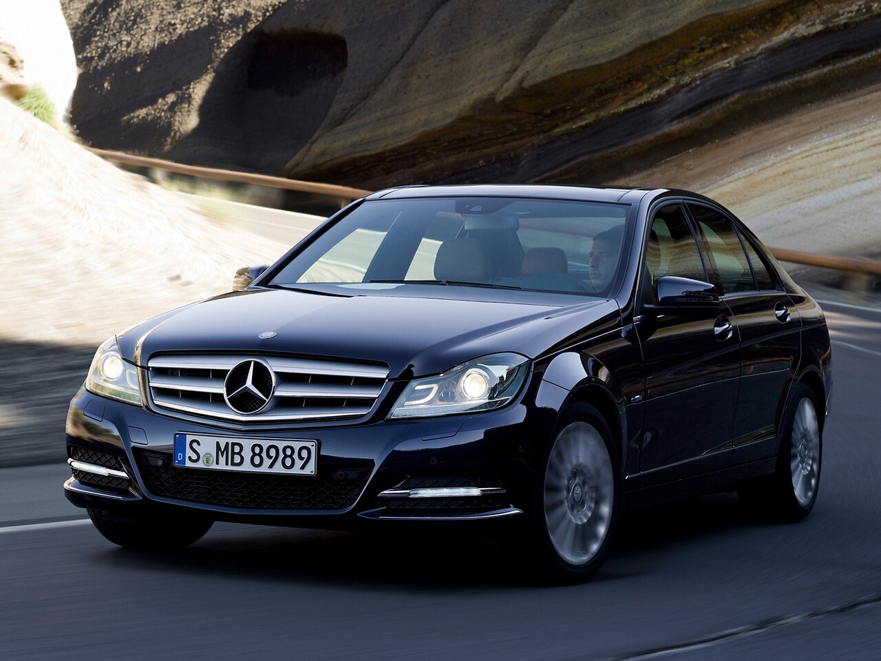 Mercedes-Benz C-Класс седан (W204 рестайлинг, 2011 - 2013 г.в.): Тёмно-синий седан на горной дороге, вид спереди сбоку
