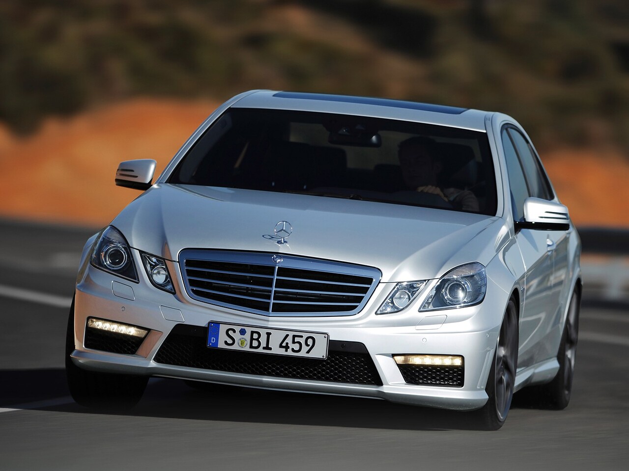 Mercedes-Benz E-Класс AMG 6.2 AT E63 AMG: Серебристый седан в движении, вид спереди сбоку