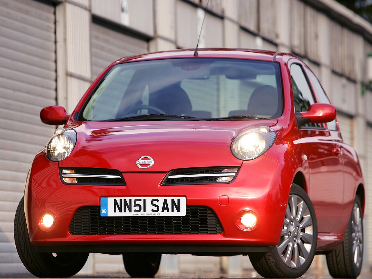 Nissan Micra хэтчбек 3-дв. (K12, 2003 - 2010 г.в.): Красный хэтчбек у городской застройки