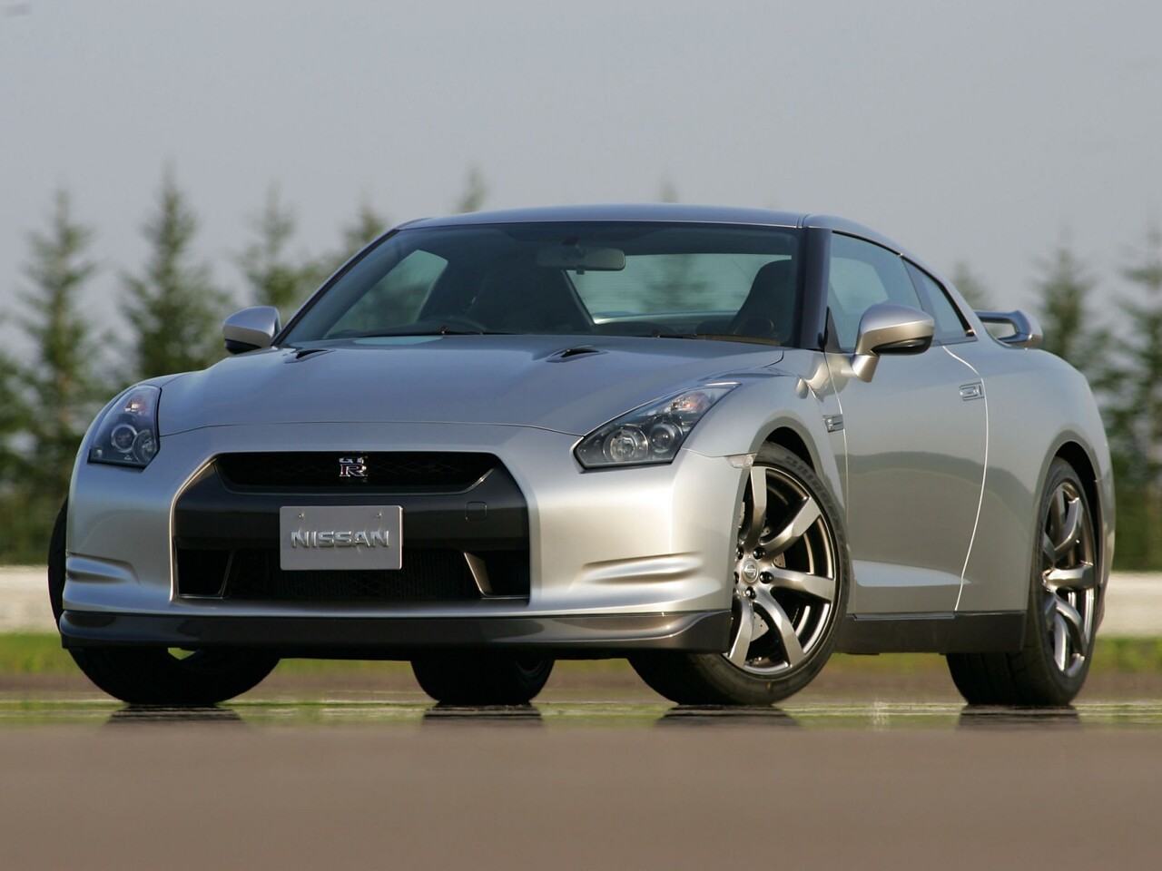 Nissan GT-R (R35, рестайлинг, 2009 - 2012 г.в.): Серебристый спорткар на фоне хвойных деревьев