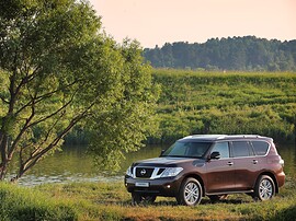 Nissan Patrol (Y62, 2010 - 2014 г.в.): Коричневый внедорожник на траве у реки на закате