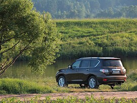 Nissan Patrol (Y62, 2010 - 2014 г.в.): Коричневый внедорожник у воды на гравийной дороге