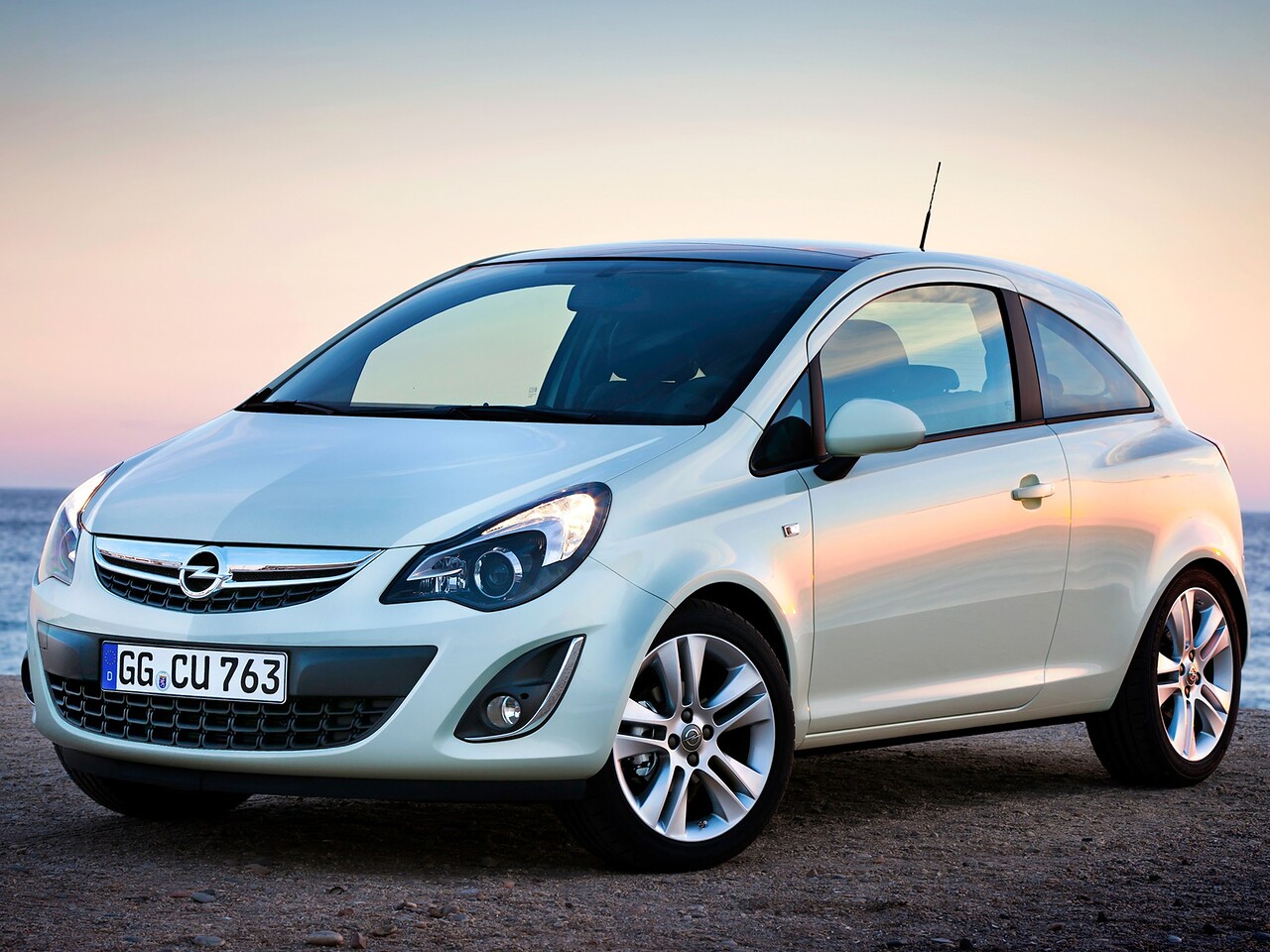 Opel Corsa 3-дв. (D 2-й рестайлинг, 2012 - 2014 г.в.): Белый трёхдверный хэтчбек на грунте на закате у воды