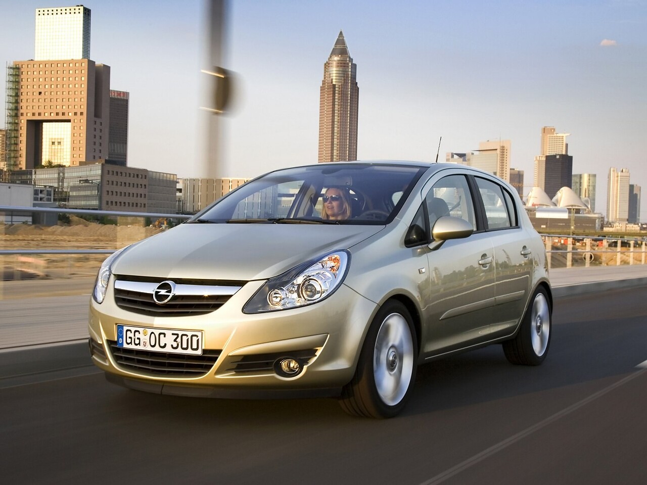 Opel Corsa хэтчбек 5-дв. (D рестайлинг, 2010 - 2012 г.в.): Золотистый хэтчбек в движении на фоне небоскрёбов