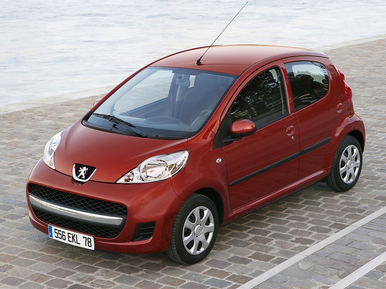 Peugeot 107 хэтчбек 5-дв. (II поколение рестайлинг, 2005 - 2012 г.в.): вид спереди и сбоку на брусчатке