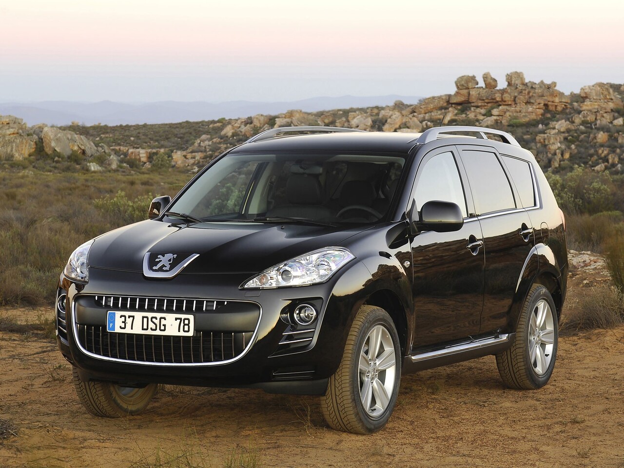 Peugeot 4007 2.0 4x4 MT Access: Три четверти спереди на грунтовой дороге у холмов
