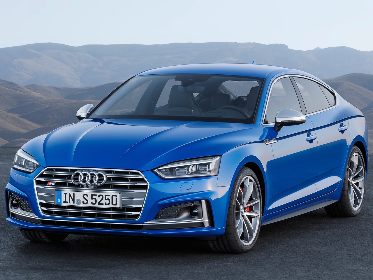 Audi S5 лифтбек (II поколение, 2016 - 2020 г.в.): Синий лифтбек на асфальте на фоне гор, вид спереди сбоку