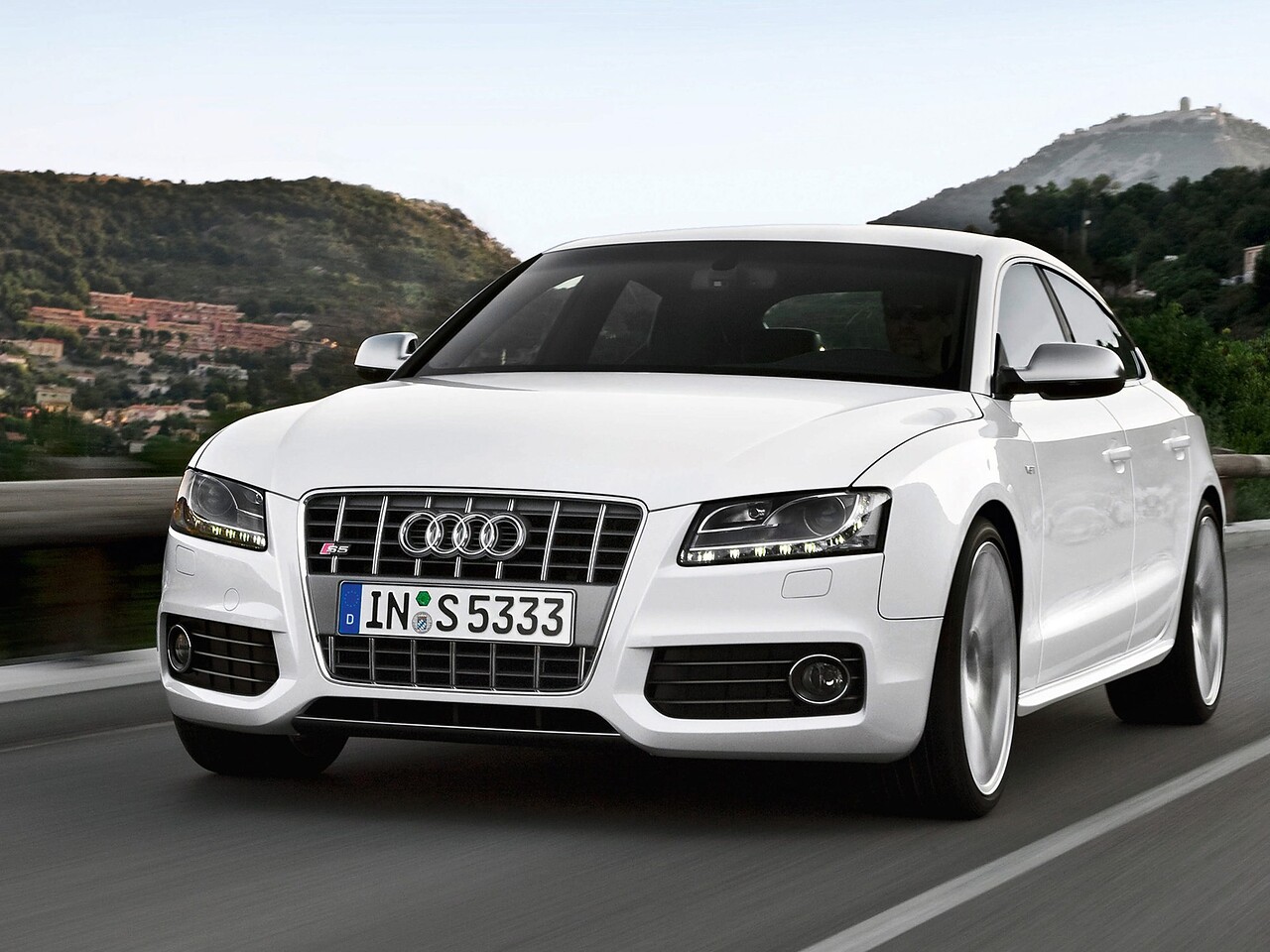 Audi S5 лифтбек (I поколение, 2009 - 2011 г.в.): Белый лифтбек на дороге у города, вид спереди сбоку