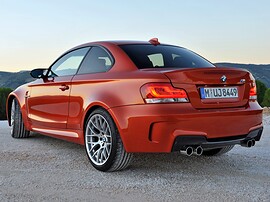 BMW 1-я серия М (E82, 2010 - 2014 г.в.): Оранжевое купе на гравии, вид сбоку сзади