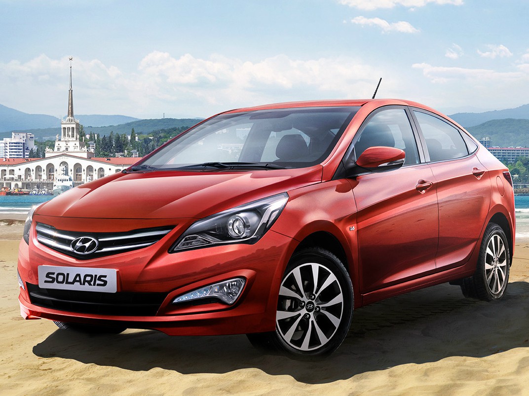 Hyundai Solaris седан (I поколение рестайлинг, 2014 - 2016 г.в.): Красный седан на песке у воды, вид спереди сбоку