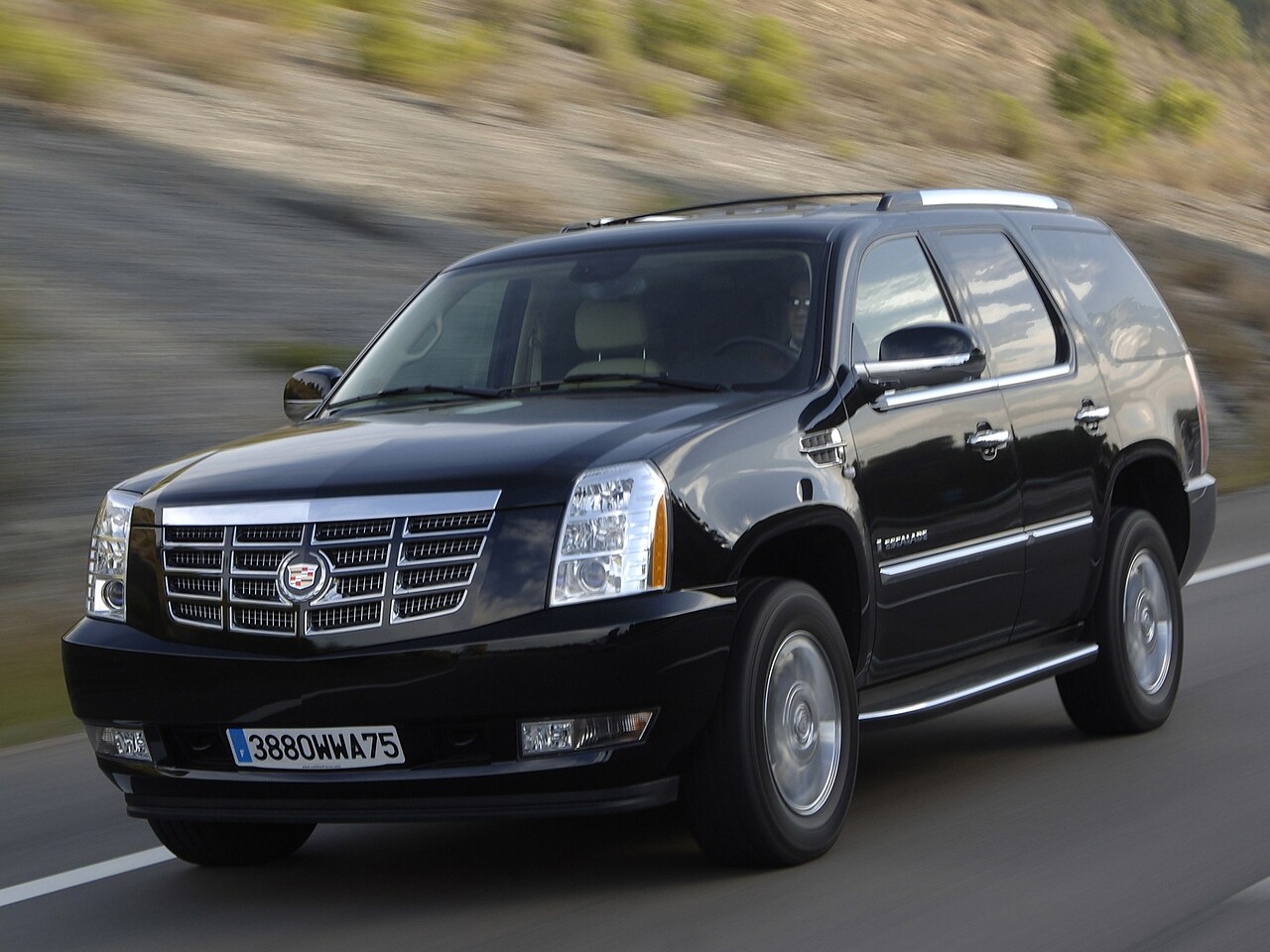 Cadillac Escalade (III поколение, 2007 - 2014 г.в.): Чёрный внедорожник на дороге на фоне холмов